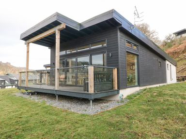 A modern black wooden house with a glass porch and wooden posts on a grassy slope at Coorie In in Aberfeldy