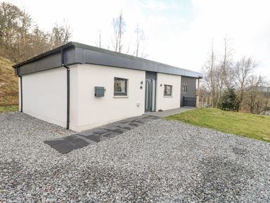 A single-story house with white and dark panel walls a gravel driveway and a path leading to the entrance at Coorie In Aberfeldy