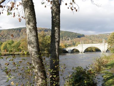 A stone bridge over a river with trees and hills in the background at Coorie In in Aberfeldy