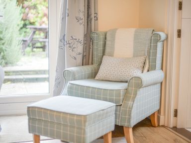 A chair with a matching ottoman and a window with floral curtains at The Old Lace Shop in Beer