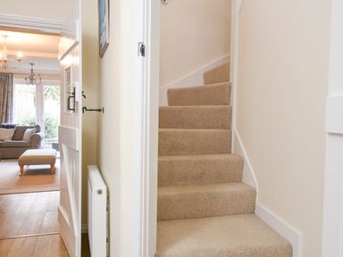 A carpeted staircase next to a hallway with an open door showing a living room with a sofa and ottoman at The Old Lace Shop in Beer