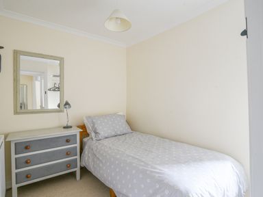 A small bedroom with a single bed covered with a patterned duvet and a dresser with a mirror on the wall at The Old Lace Shop in Beer