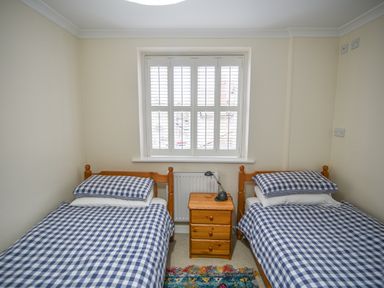 A bedroom with two single beds with blue and white checkered bedding and a wooden nightstand with a lamp between them at The Old Lace Shop in Beer