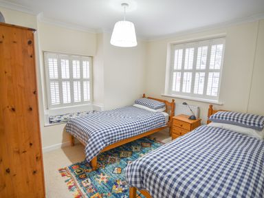 A bedroom with two single beds covered in blue check bedding a wooden wardrobe and a colorful rug at The Old Lace Shop in Beer