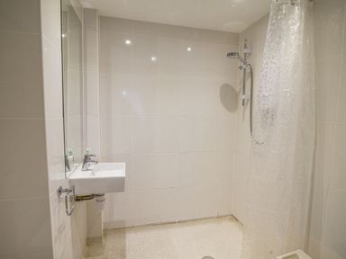 A bathroom with a wall-mounted sink and a shower area with a showerhead and a translucent curtain at The Old Lace Shop in Beer