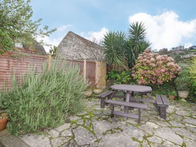 A garden patio with a wooden picnic table surrounded by plants and a wooden fence at The Old Lace Shop in Beer