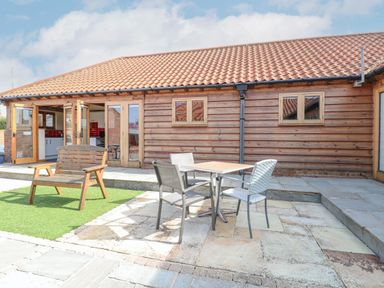 An outdoor patio area with a wooden bench and a table with three chairs in front of a wooden building at 5a Hideaways in Hunstanton