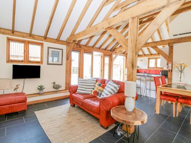A living area with a red leather sofa and chair wooden beams and a dining table with red chairs at 5a Hideaways in Hunstanton