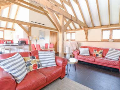A living room with red sofas, striped and patterned cushions, wooden beams, a small round table with a lamp, and a dining area with red chairs at 5a Hideaways Hunstanton