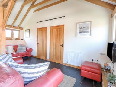 A living room with red leather sofas wooden doors and beams and a wall-mounted television at 5a Hideaways in Hunstanton