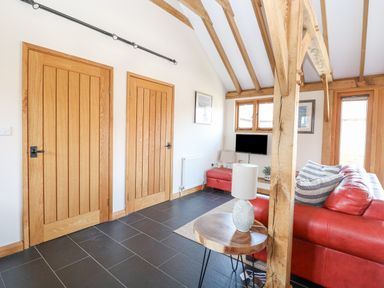 A living room with wooden doors beams a red sofa a side table with a lamp and a wall mounted television at 5a Hideaways in Hunstanton