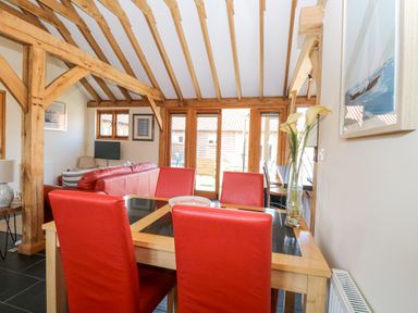 A dining area with a wooden table and red chairs next to a living room with a red sofa and wooden beams at 5a Hideaways Hunstanton