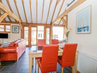 A dining area with a wooden table and red chairs next to a living room with red sofas and wooden beams at 5a Hideaways in Hunstanton