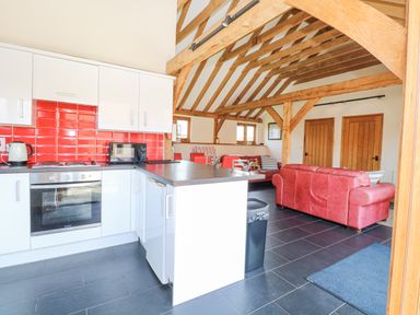A kitchen with white cabinets red backsplash and black countertop next to a living area with red sofas and wooden beams at 5a Hideaways in Hunstanton
