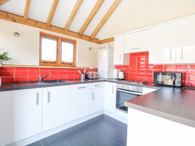 A kitchen with white cabinets red tiled backsplash wooden beams and appliances at 5a Hideaways in Hunstanton