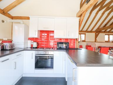 A kitchen with white cabinets red tile backsplash and wooden beams at 5a Hideaways in Hunstanton