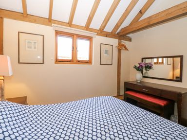 A bedroom with a patterned bedspread a wooden dresser with a mirror and flowers and exposed wooden beams at 5a Hideaways in Hunstanton