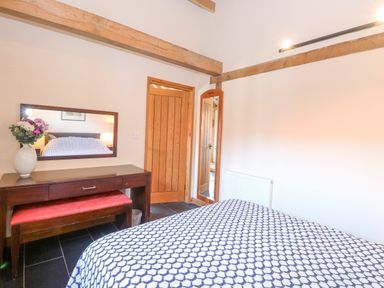 A bedroom with a bed covered in patterned bedding a wooden dresser with mirror and flowers and a wooden door at 5a Hideaways in Hunstanton