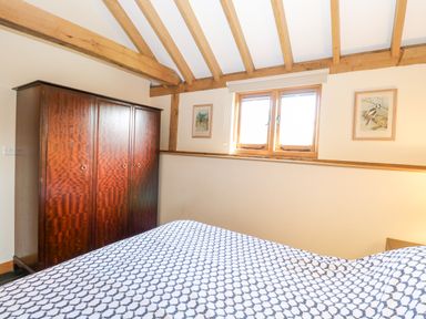 A bedroom with a wooden wardrobe a bed with patterned bedding and two framed pictures by a window at 5a Hideaways in Hunstanton