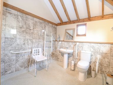 A bathroom with a toilet sink chair grab bars and tiled walls at 5a Hideaways in Hunstanton