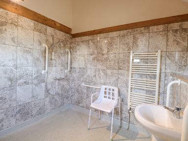 A bathroom with a shower area with grab bars a white chair a towel rack and a sink at 5a Hideaways in Hunstanton