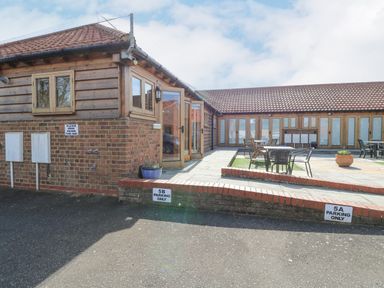 An outdoor patio area with tables and chairs next to a building with wooden and brick walls at 5a Hideaways in Hunstanton