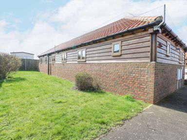 An exterior view of a building with brick and wood siding with a grassy area and bushes at 5a Hideaways in Hunstanton