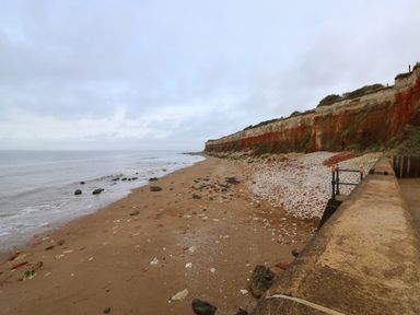 A sandy beach with scattered rocks next to cliffs and a concrete walkway at 5a Hideaways in Hunstanton