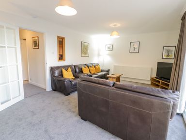 A living room with brown leather sofas and yellow cushions a wooden coffee table a television on a wooden stand and framed pictures on walls at Borthwen in Barmouth
