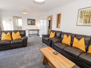 A living room with two brown leather sofas with yellow cushions a wooden coffee table and a wooden desk against the wall at Borthwen in Barmouth