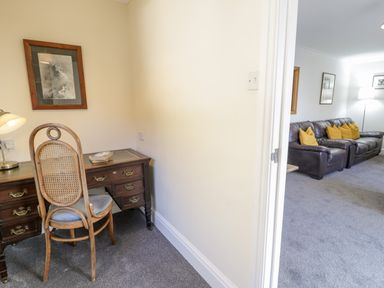 A small study area with a wooden desk and chair and a lamp next to a living room with a brown sofa and yellow cushions at Borthwen in Barmouth