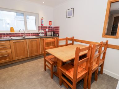 A kitchen with wooden cabinets a wooden dining table with six chairs and red tiled backsplash at Borthwen in Barmouth