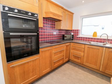 A kitchen with wooden cabinets a built-in double oven a microwave a sink and a window with a yellow jug on the sill at Borthwen in Barmouth