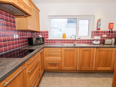 A kitchen with wooden cabinets red tiled backsplash a window a sink an electric stove a microwave a toaster and a kettle at Borthwen in Barmouth