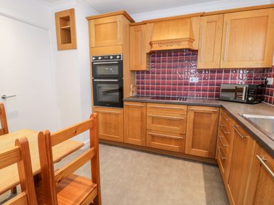 A kitchen with wooden cabinets and a dining table with chairs at Borthwen in Barmouth