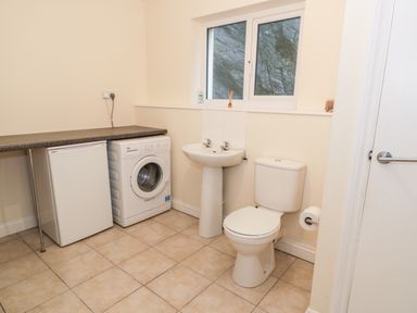 A room with a washing machine fridge toilet and sink under a window at Borthwen in Barmouth