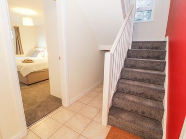 A stairway with grey carpet next to a tiled floor hallway and an open door revealing a bedroom at Borthwen in Barmouth