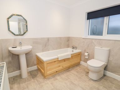 A bathroom with a sink, bathtub with wooden panel, toilet, and a window with a dark blind at Borthwen in Barmouth