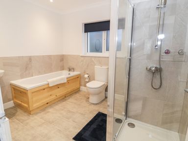 A bathroom with a wooden bathtub panel toilet shower enclosure and a window at Borthwen in Barmouth