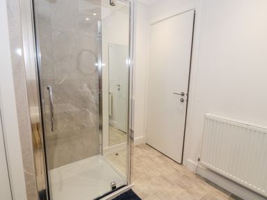 A shower with glass doors and a door next to a radiator in a tiled bathroom at Borthwen in Barmouth