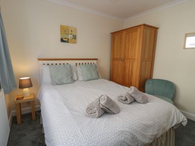 A bedroom with a bed with pillows and towels a wooden wardrobe a bedside table with lamp and a green chair at Borthwen in Barmouth