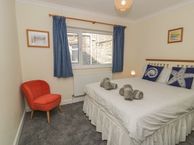 A bedroom with a double bed with rolled towels on it a red chair blue curtains and pictures on the walls at Borthwen in Barmouth