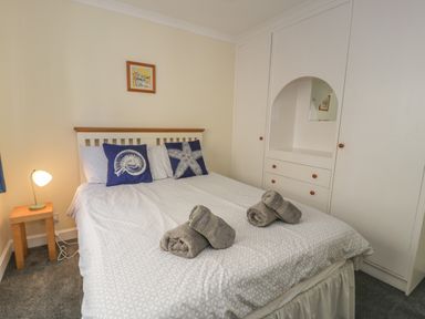 A bedroom with a double bed with patterned bedding and decorative cushions a bedside lamp on a wooden table and built in white wardrobe in Borthwen Barmouth