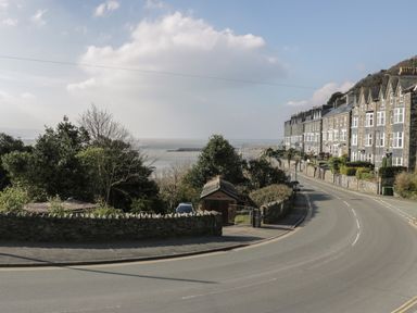 A coastal road with stone houses on the right and trees on the left overlooking the sea at Borthwen in Barmouth