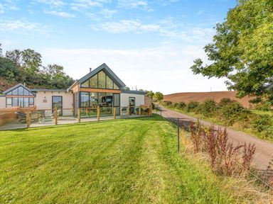 A house with large windows and a glass railing on a grassy lawn next to a rural road at Shearwater Lodge Bamburgh