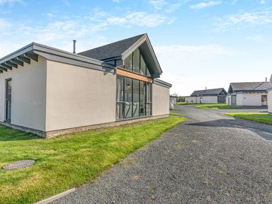 A cluster of modern single story houses with large windows and a gravel road at Shearwater Lodge in Bamburgh