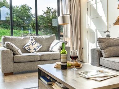 A living room with two grey sofas a coffee table with wine and snacks near large windows at Shearwater Lodge in Bamburgh