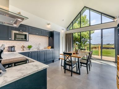 A kitchen with dark cabinets and marble countertops next to a dining table and large windows at Shearwater Lodge in Bamburgh