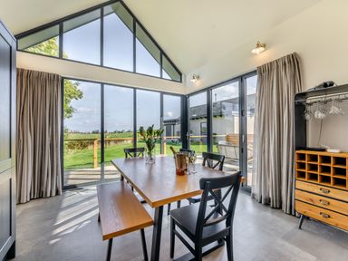 A dining area with a wooden table, benches, chairs and large windows overlooking a green field at Shearwater Lodge in Bamburgh