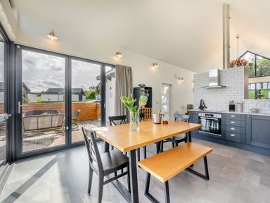 A kitchen and dining area with a wooden table black chairs and a bench next to sliding glass doors leading to a patio at Shearwater Lodge in Bamburgh